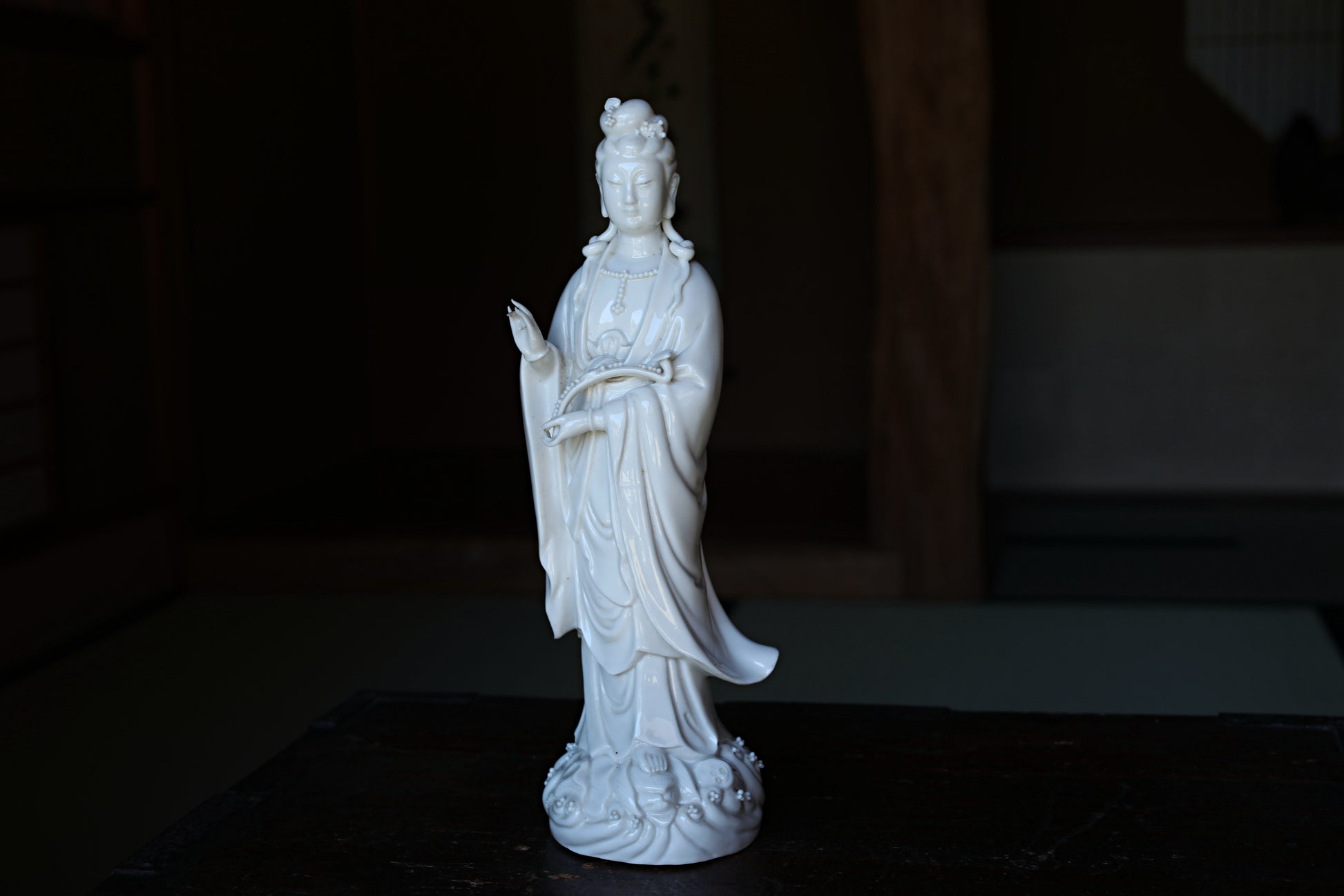 A white ceramic statue of a deity, possibly a Buddha, standing on a wooden surface.