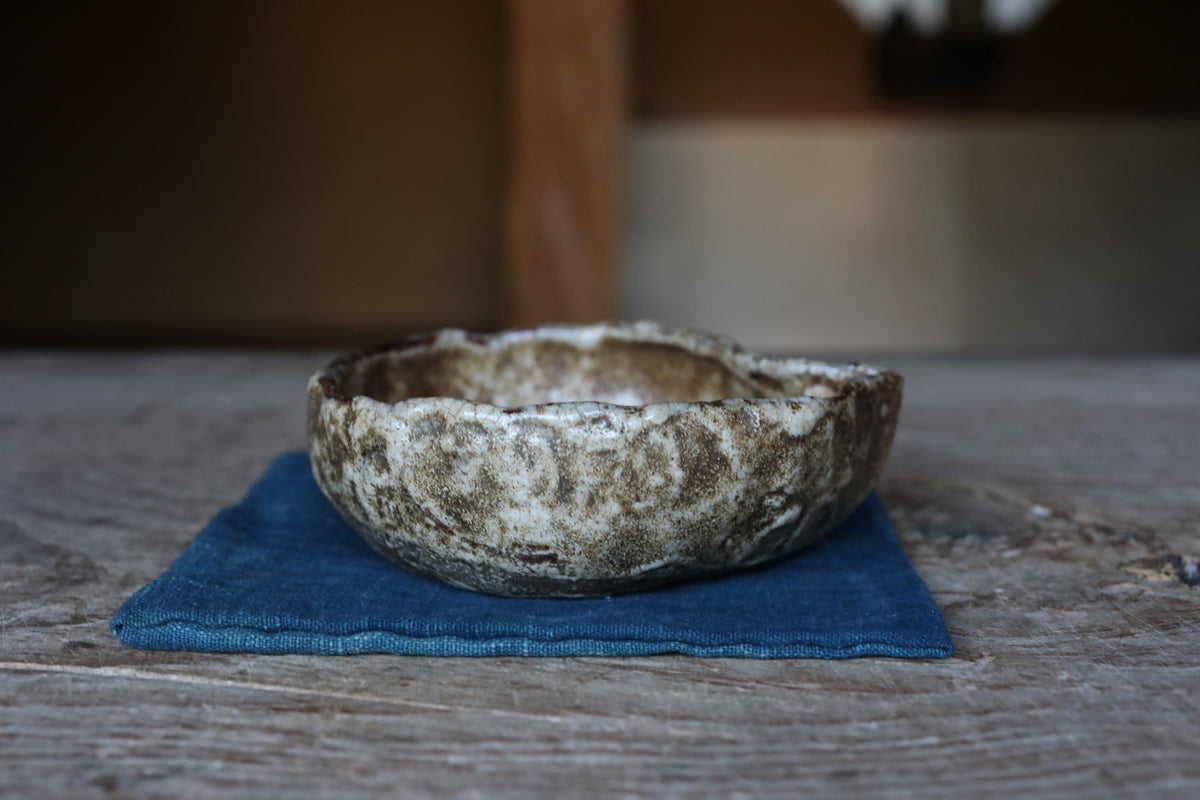A ceramic bowl with a textured surface sits on a blue cloth on a wooden surface.