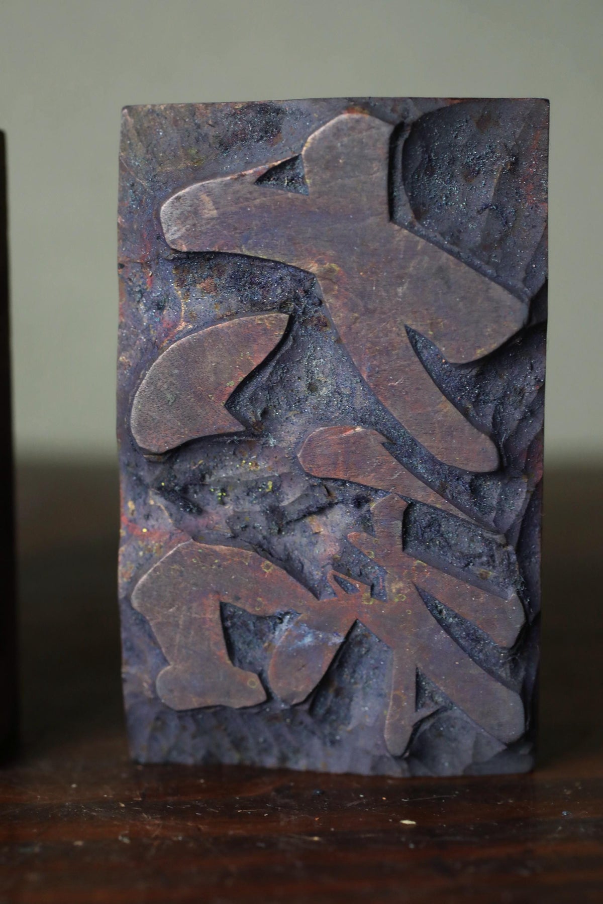 a dark-colored, textured stone or metal object with a stylized, abstract design or symbol carved into it.