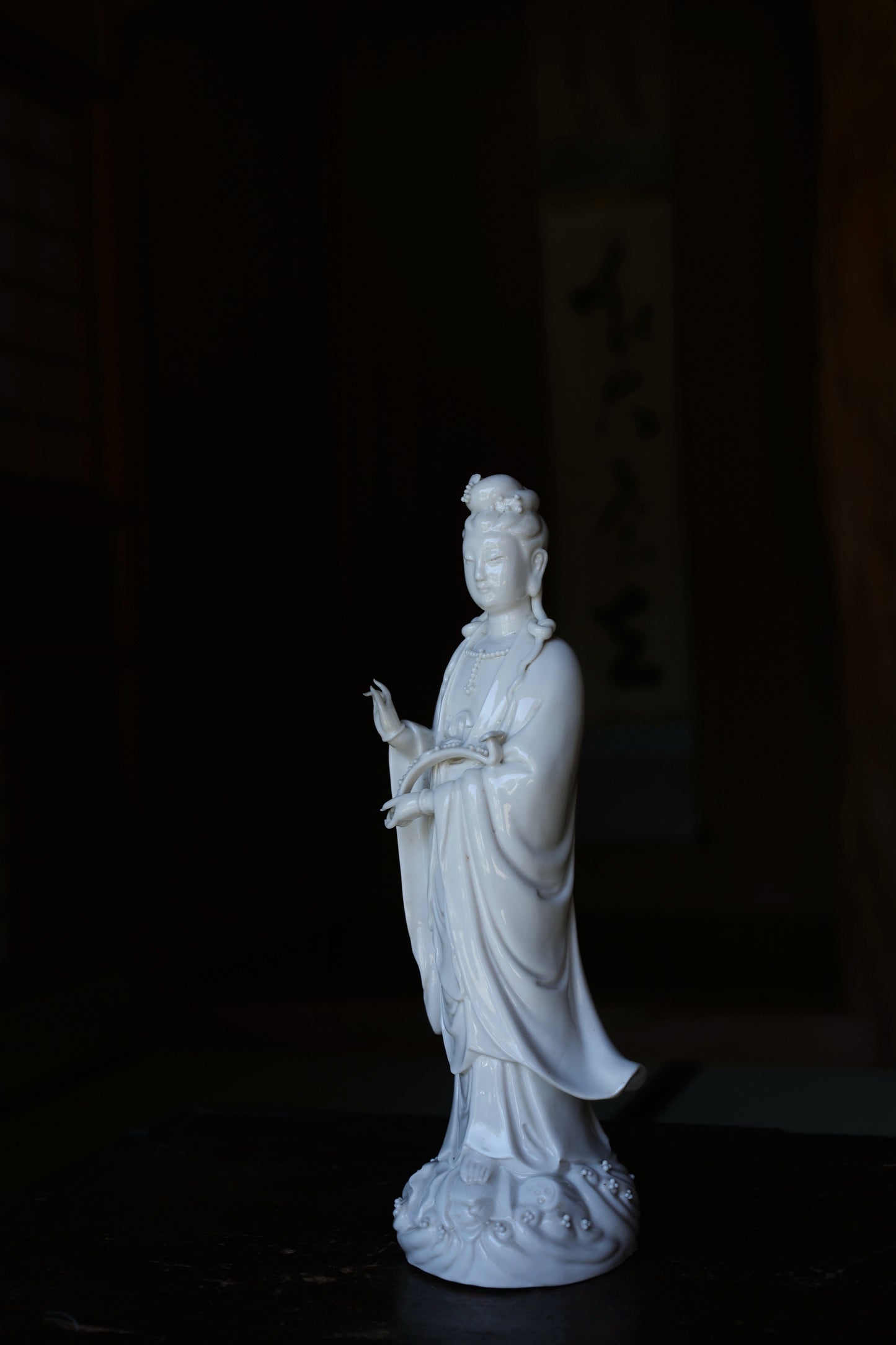 A white ceramic statue of a person, possibly a deity, standing on a dark surface.