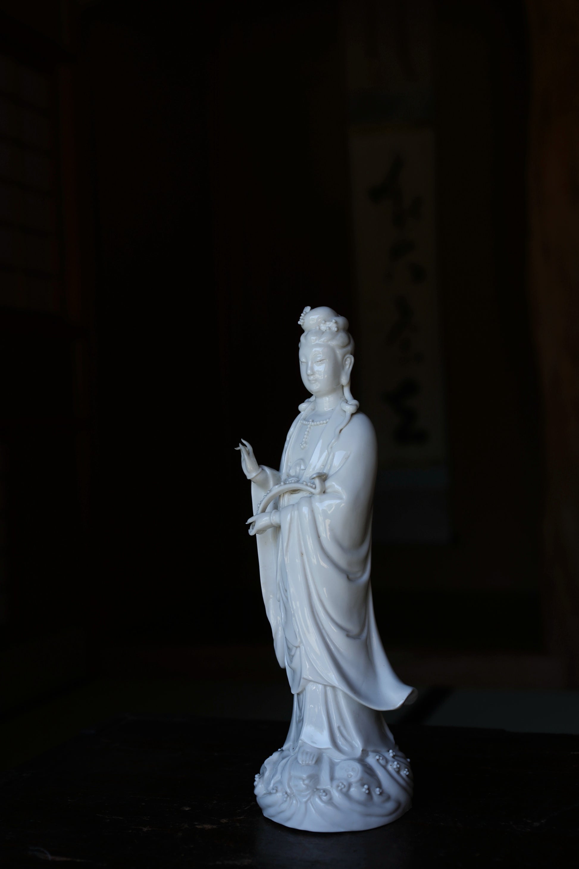 A white ceramic statue of a person, possibly a deity, standing on a dark surface.