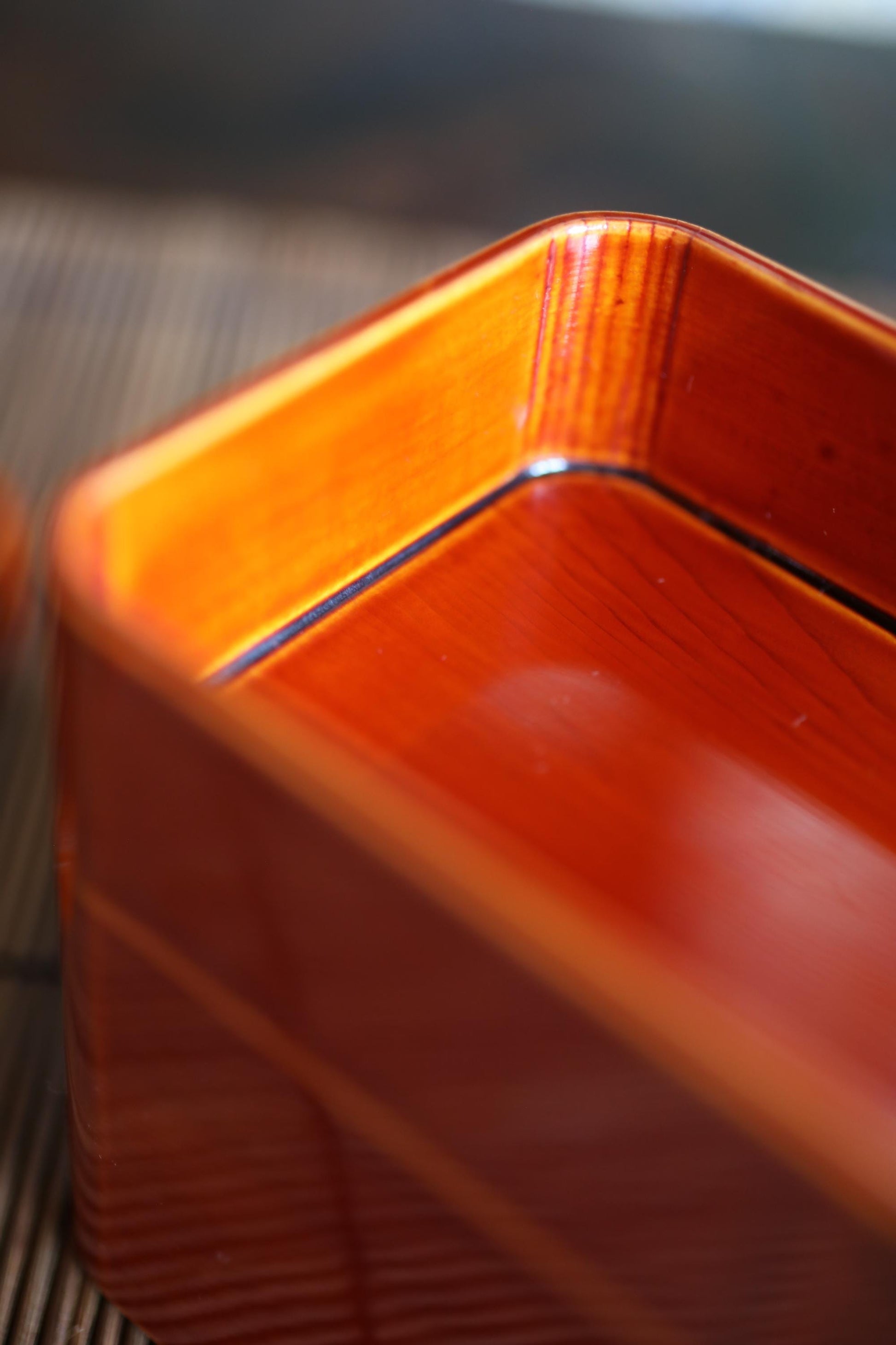 A close-up view of a wooden object with a warm, orange-red hue, possibly a piece of furniture or a decorative item.