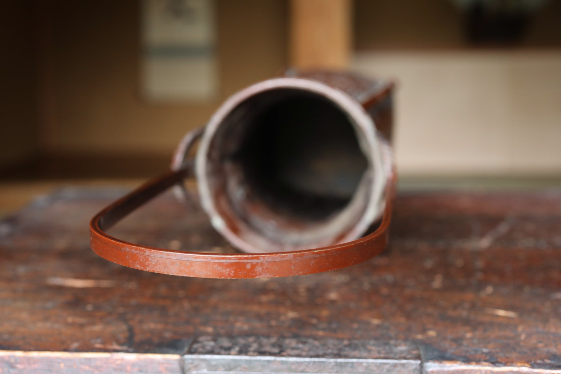 An old, rusted metal bucket with a handle is placed on a wooden surface.