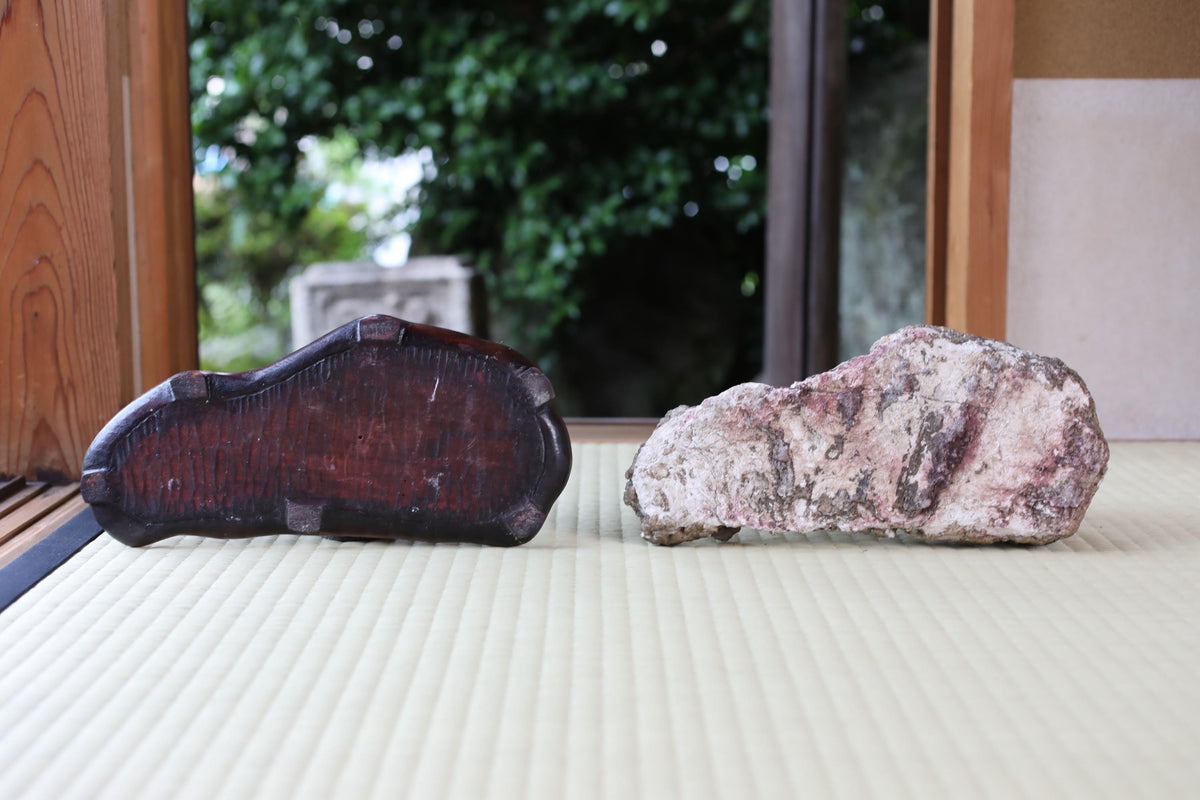 a pair of wooden shoes and a large rock placed on a white surface, with a blurred background of trees.