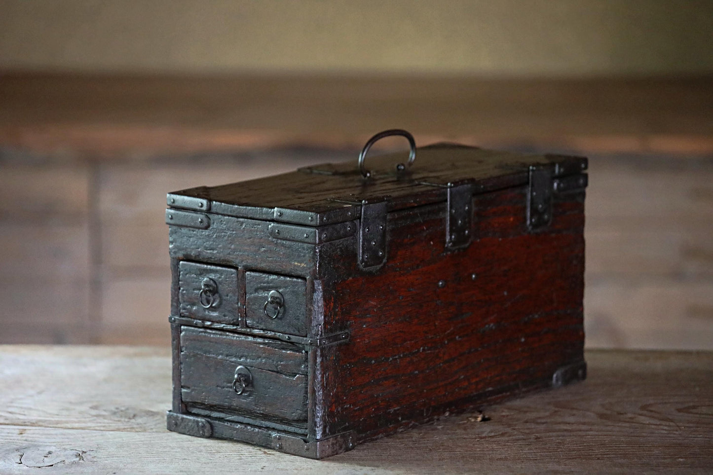 An old, wooden chest with metal clasps sits on a wooden surface.