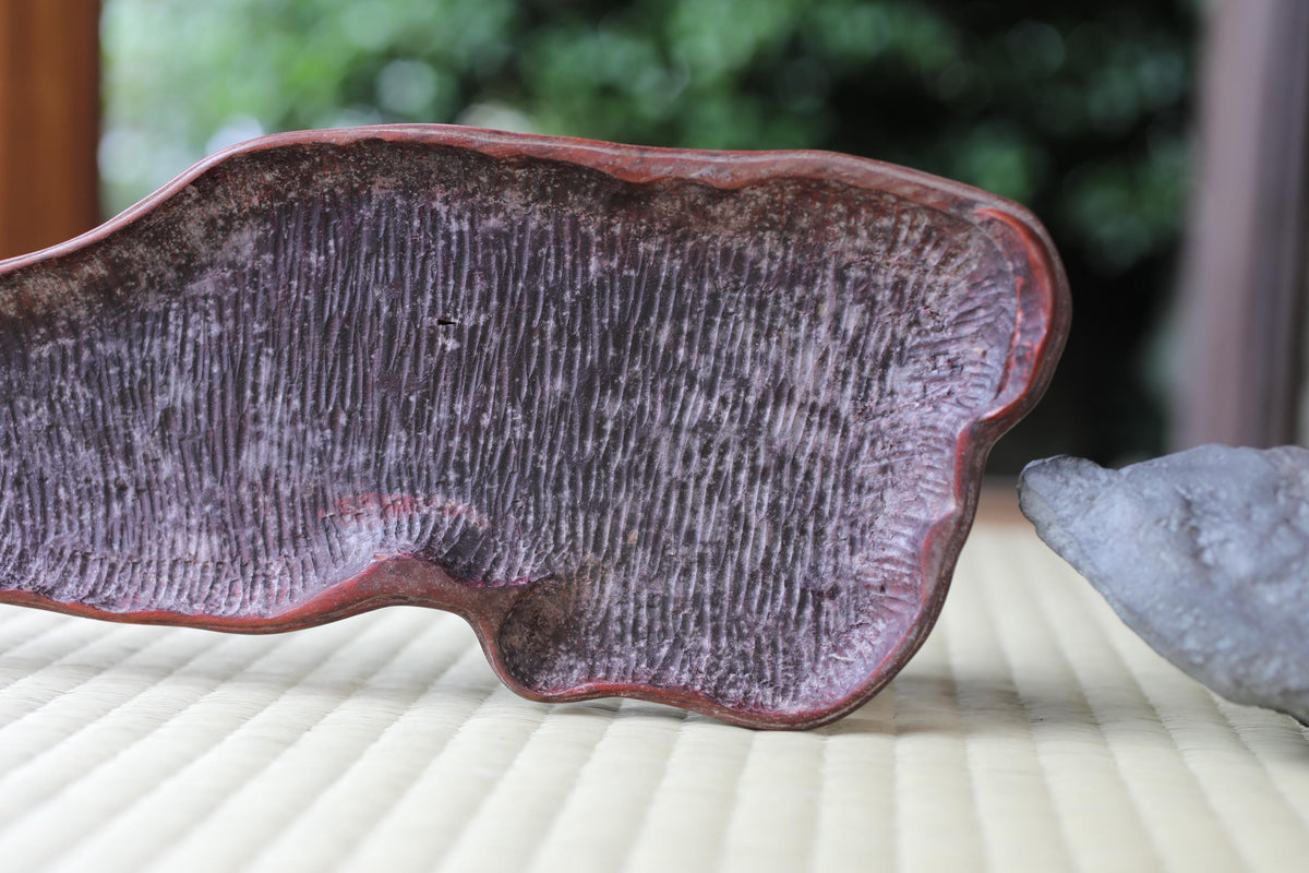 a close-up view of a textured, reddish-brown object, possibly a piece of pottery or a sculpture, placed on a white surface.