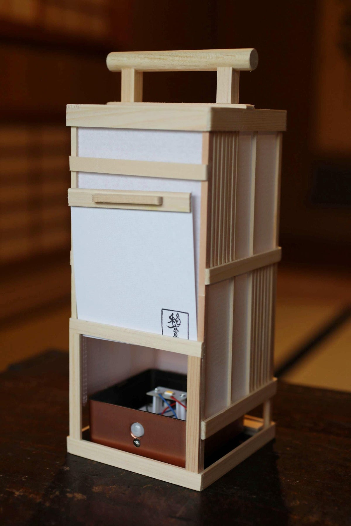 A wooden box with a handle on top, featuring a small compartment at the bottom.