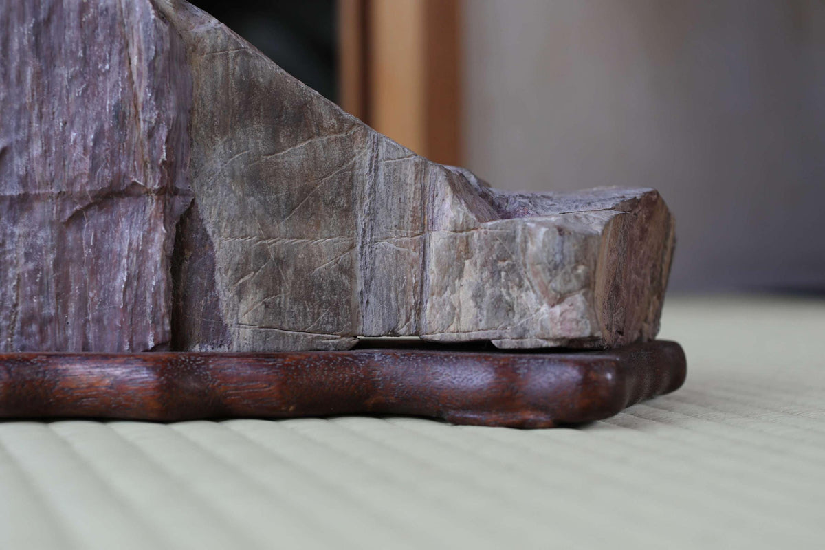 A close-up image of a wooden base holding a large, irregularly shaped piece of wood, possibly a piece of driftwood or a carved wooden object.