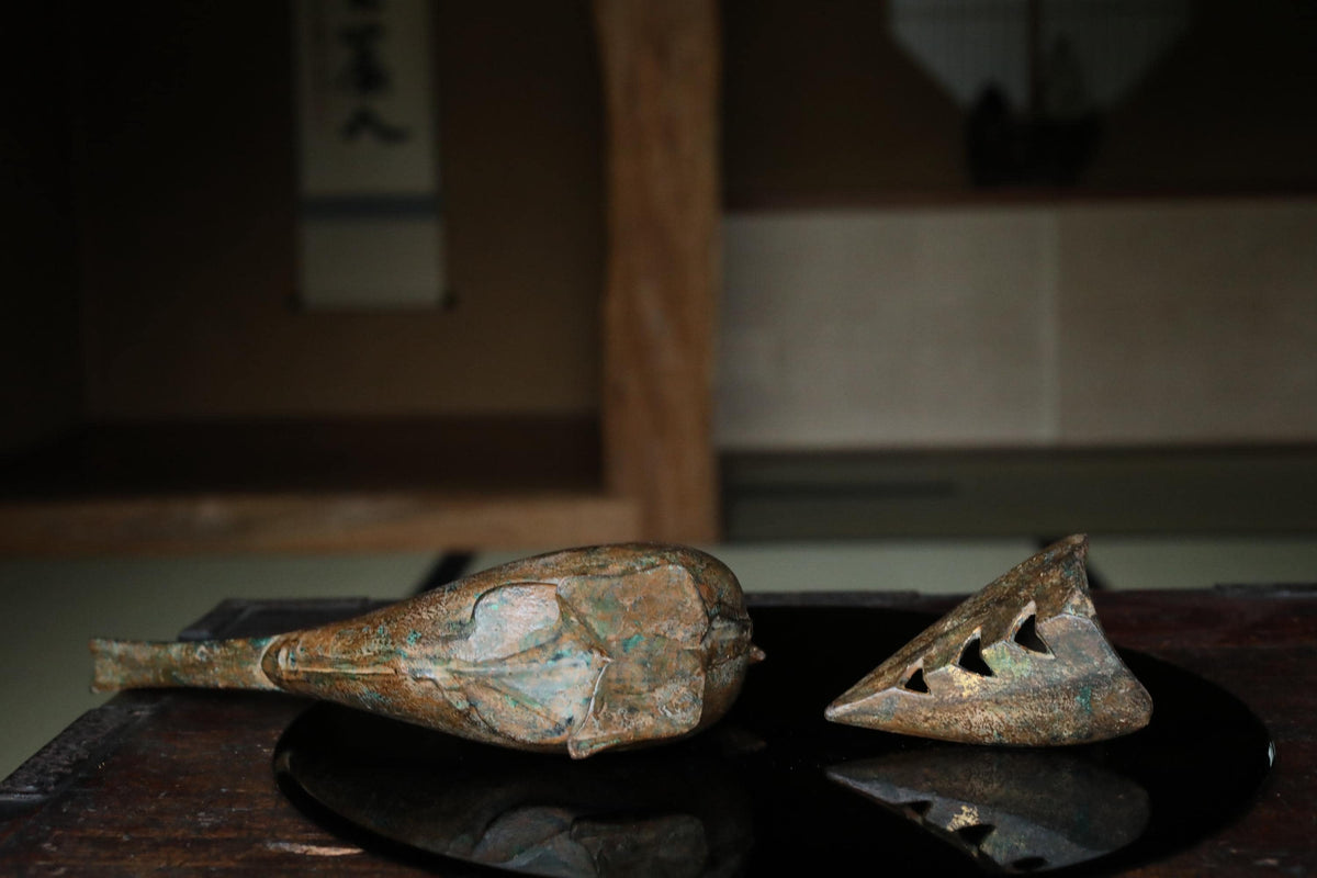 two antique metal objects, one larger and one smaller, resting on a reflective surface.
