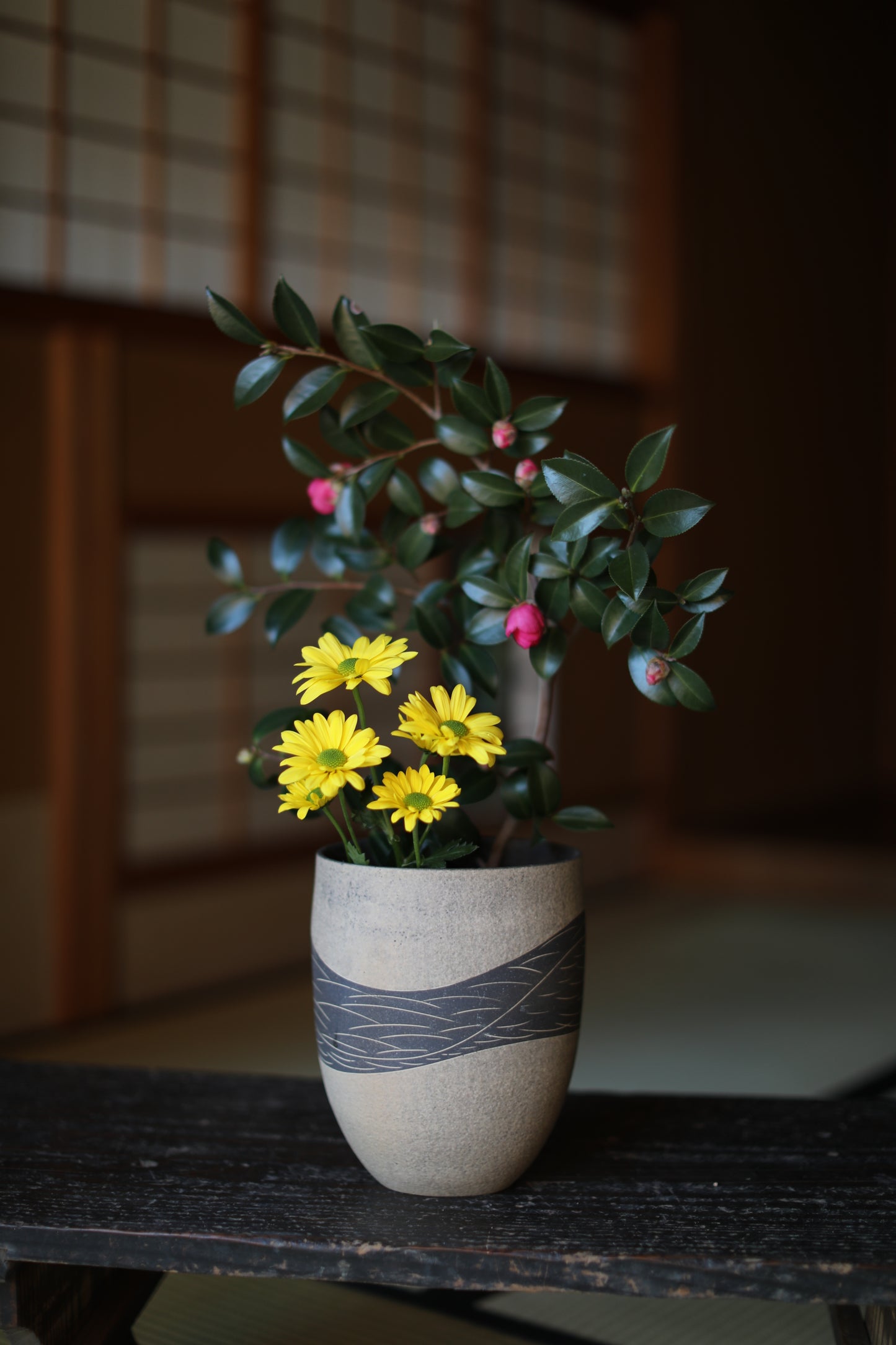 A ceramic pot with a striped pattern holds a small plant with yellow flowers and green leaves.
