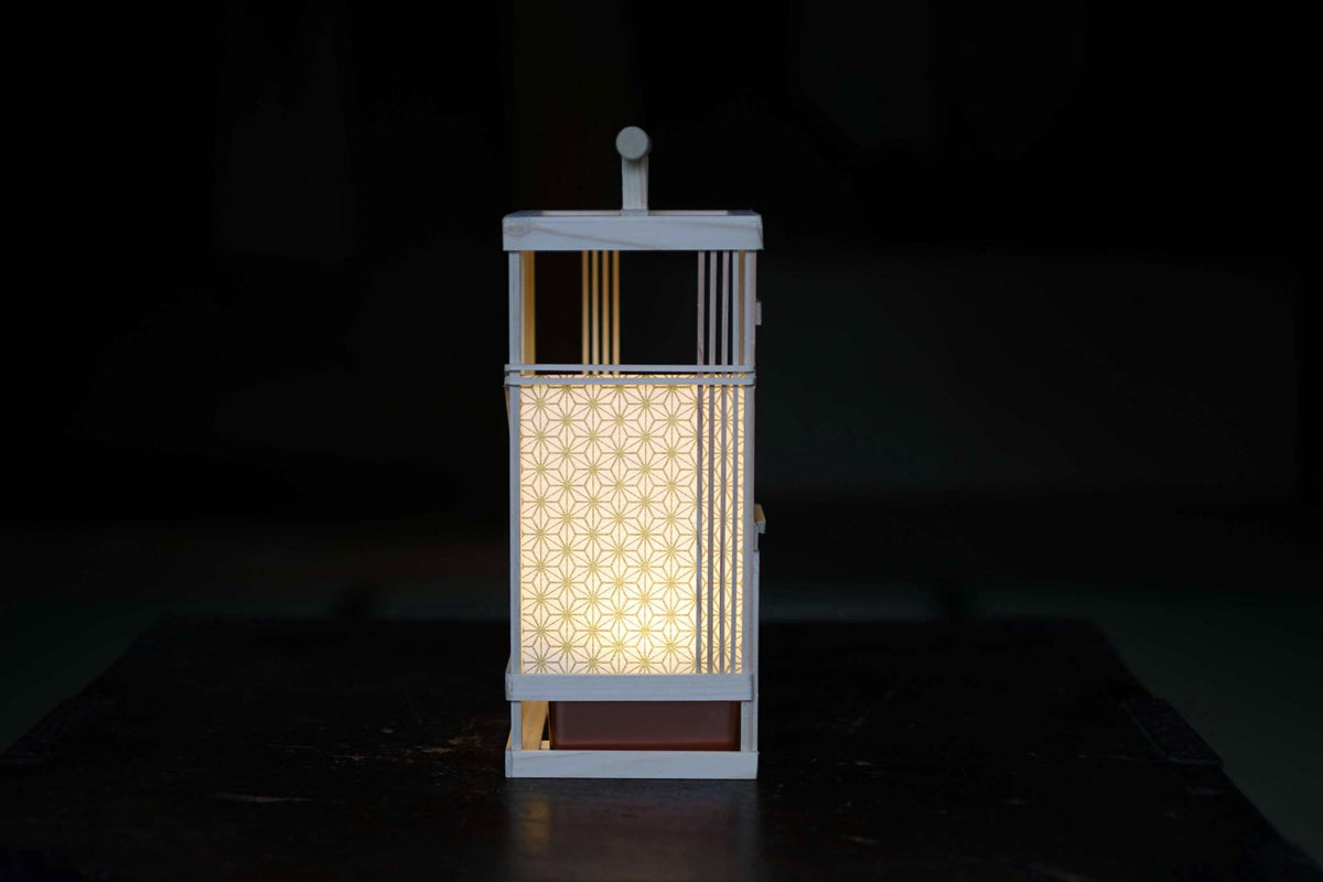 A white lantern with a patterned light inside is illuminated against a dark background.