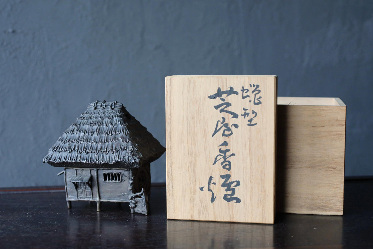 a small, intricately designed miniature house next to a wooden box with Japanese text on it.