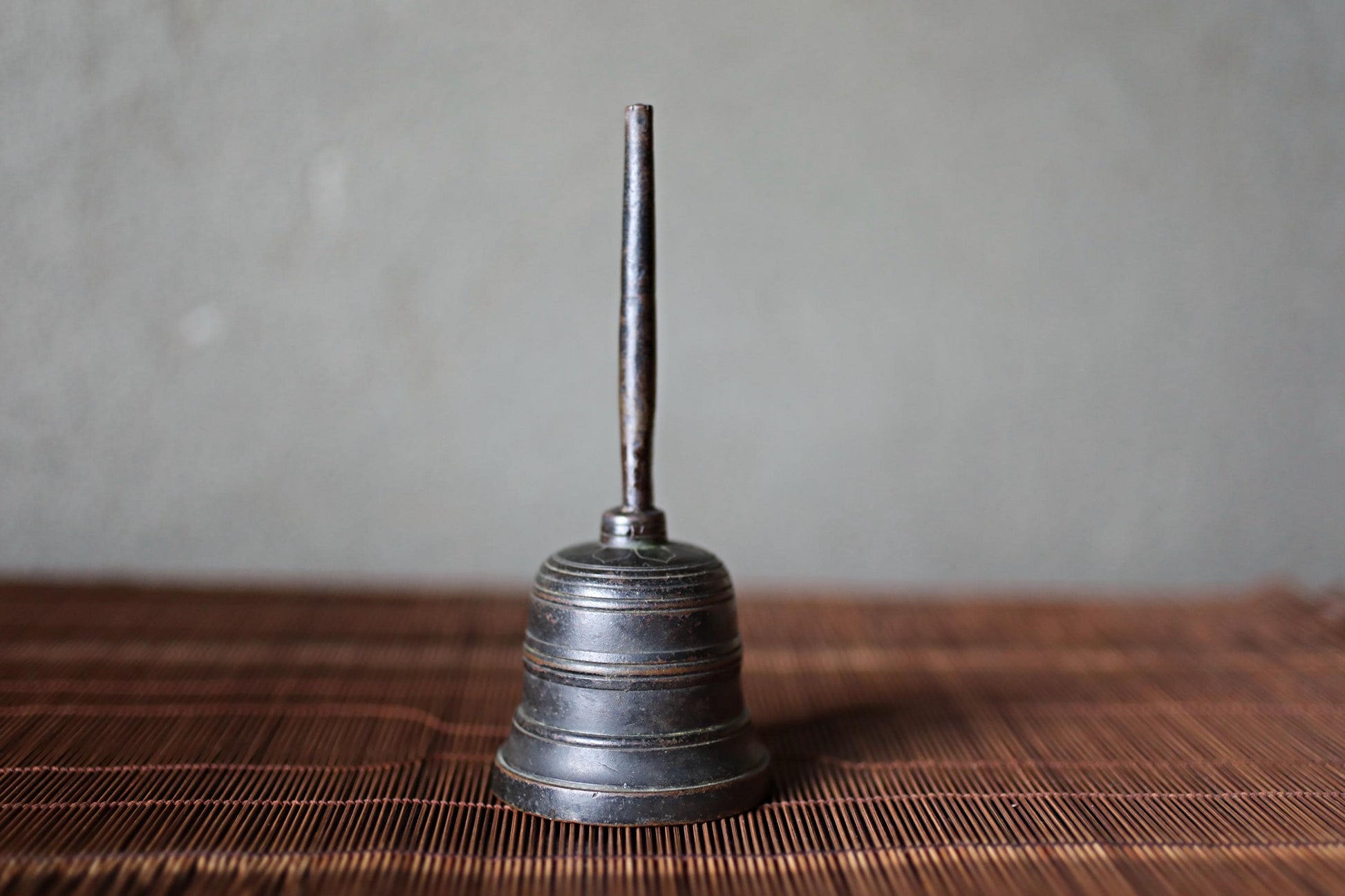 A metal bell with a long, thin handle is sitting on a wooden surface.
