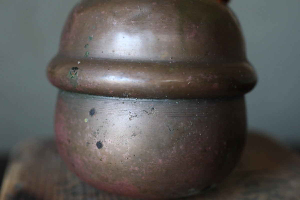 A close-up image of a rusted, antique-looking metal container or vase with a textured, weathered appearance.