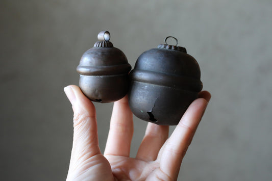 A hand holding two antique-looking black metal bells against a plain background.