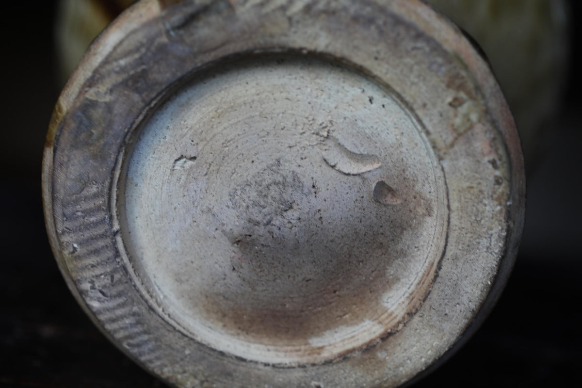 A close-up view of a ceramic or metal object, possibly a vase or container, with a textured surface and a circular shape.