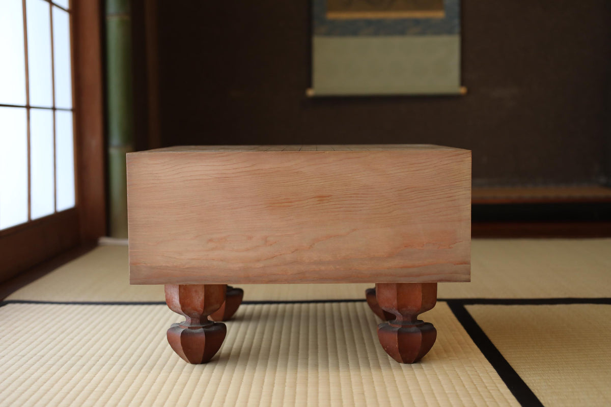A wooden table with four legs, placed on a tatami mat in a room with a window and a painting on the wall.