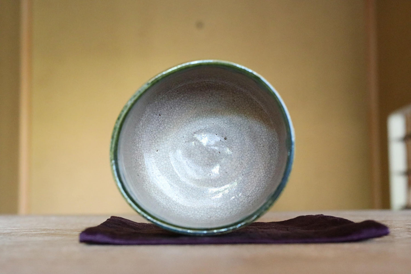 A ceramic bowl with a green rim sits on a purple cloth on a wooden surface.