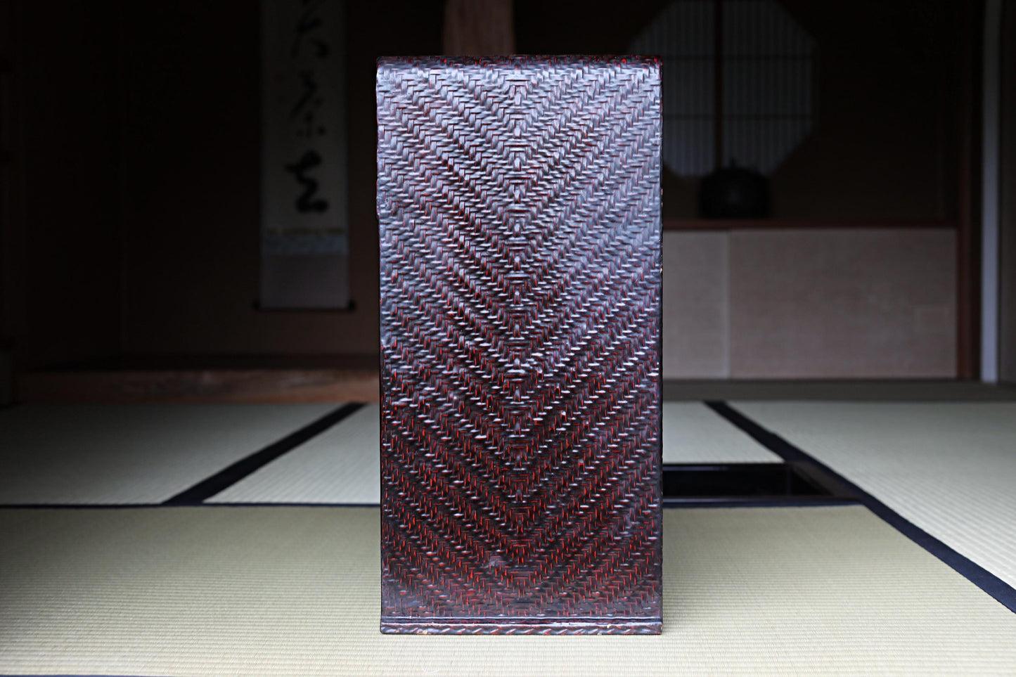 a dark brown woven object with a zigzag pattern, placed on a white mat with a black border.