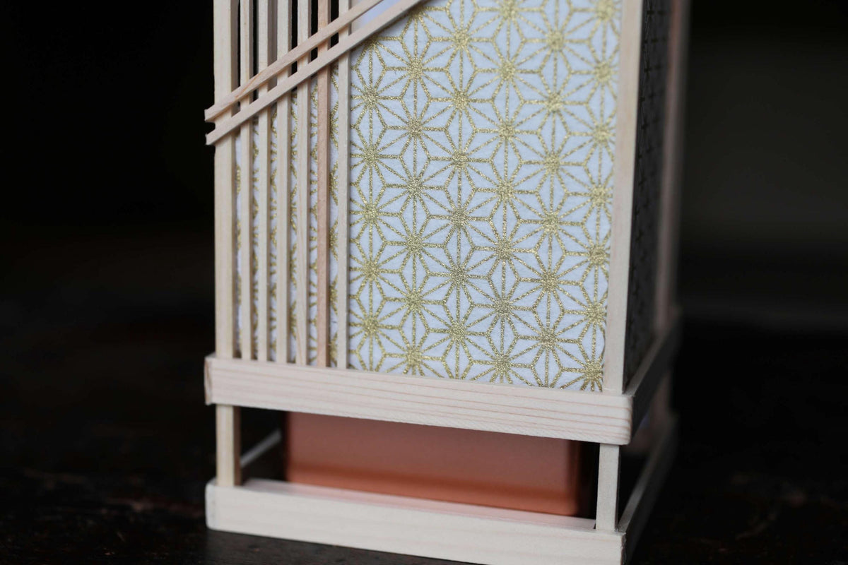 A wooden lantern with a white and gold patterned paper covering, featuring a wooden frame and a red base.