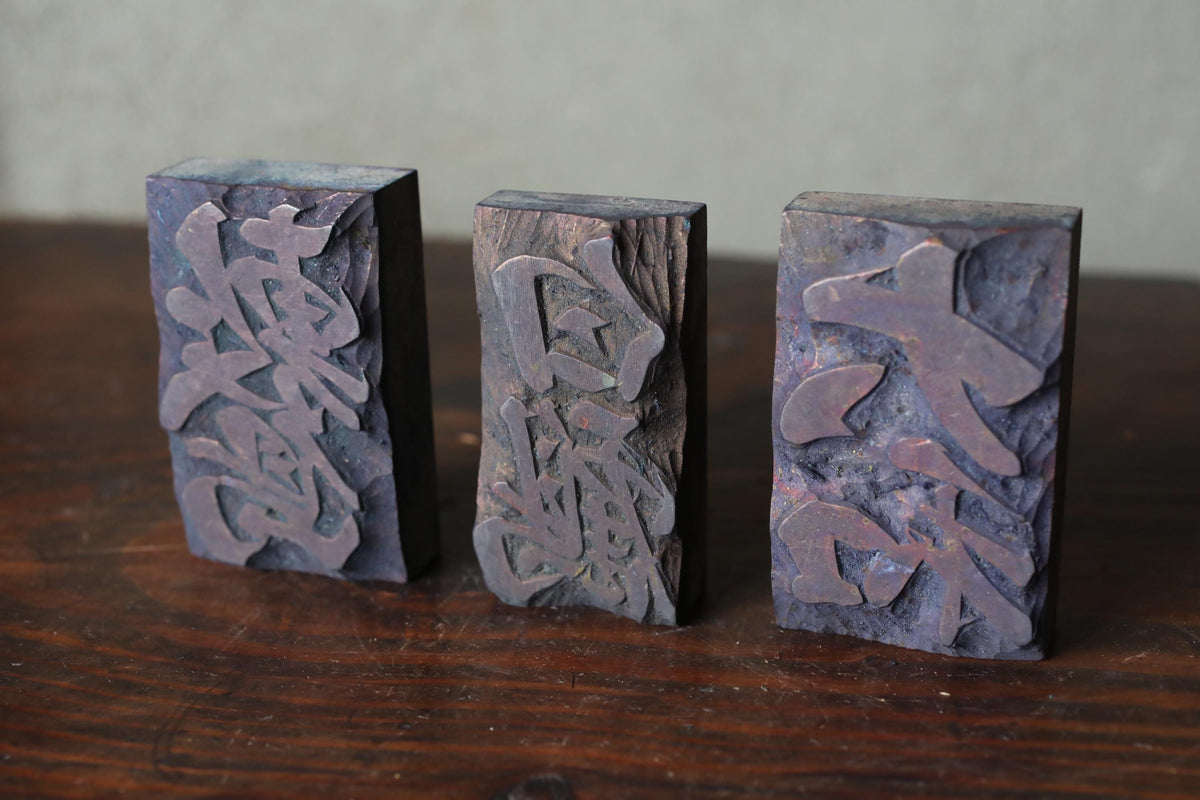 Three rectangular metal blocks with intricate designs carved into them, placed on a wooden surface.