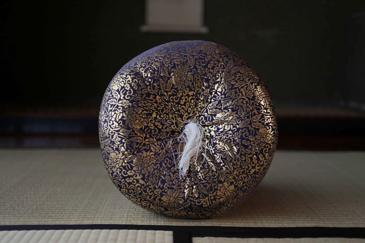 A decorative blue and gold object with a white tassel, placed on a woven mat against a dark background.