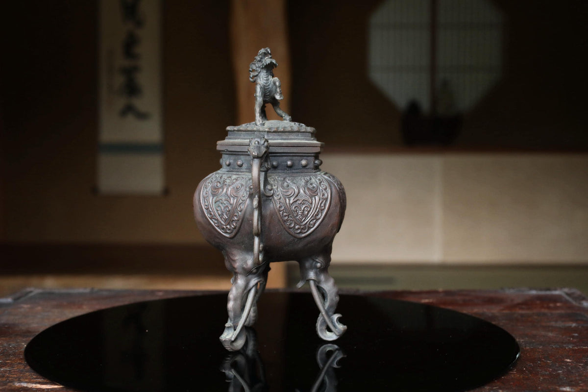 a decorative metal object, possibly a vase or urn, placed on a reflective surface.