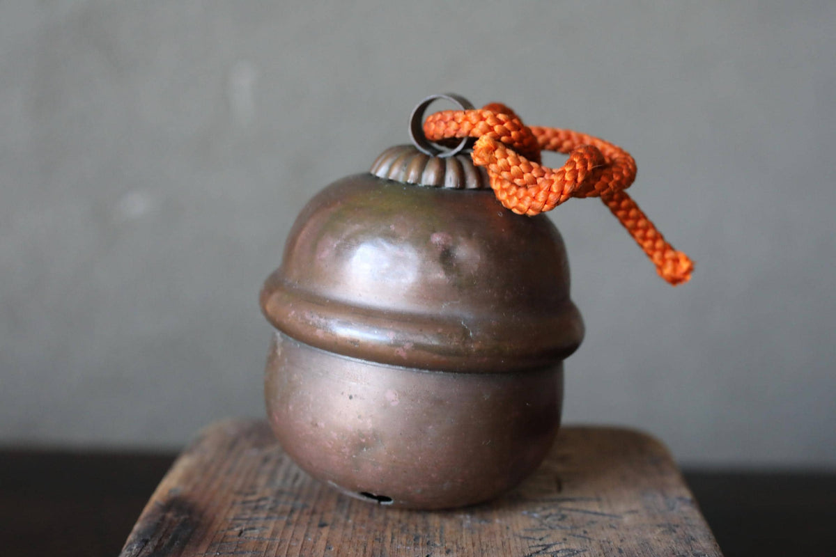 A round, metallic bell with a rope tied around it, sitting on a wooden surface against a gray background.