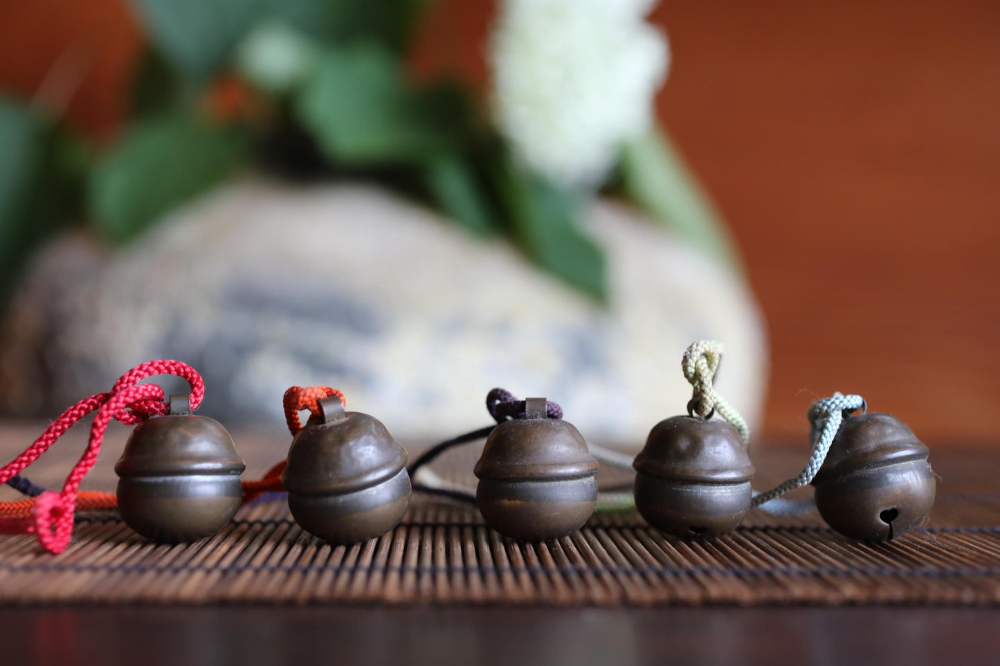 A row of five small, round metal bells with colorful strings attached, arranged on a wooden surface.