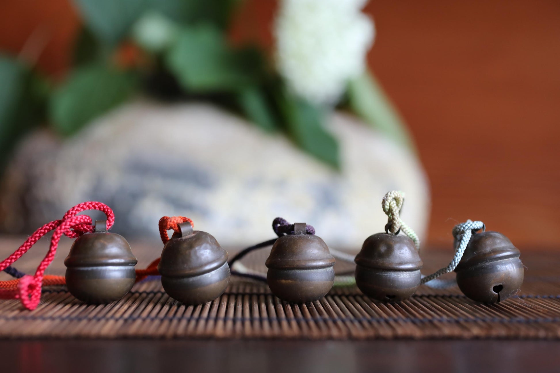 A row of five small, round metal bells with colorful strings attached, arranged on a wooden surface.