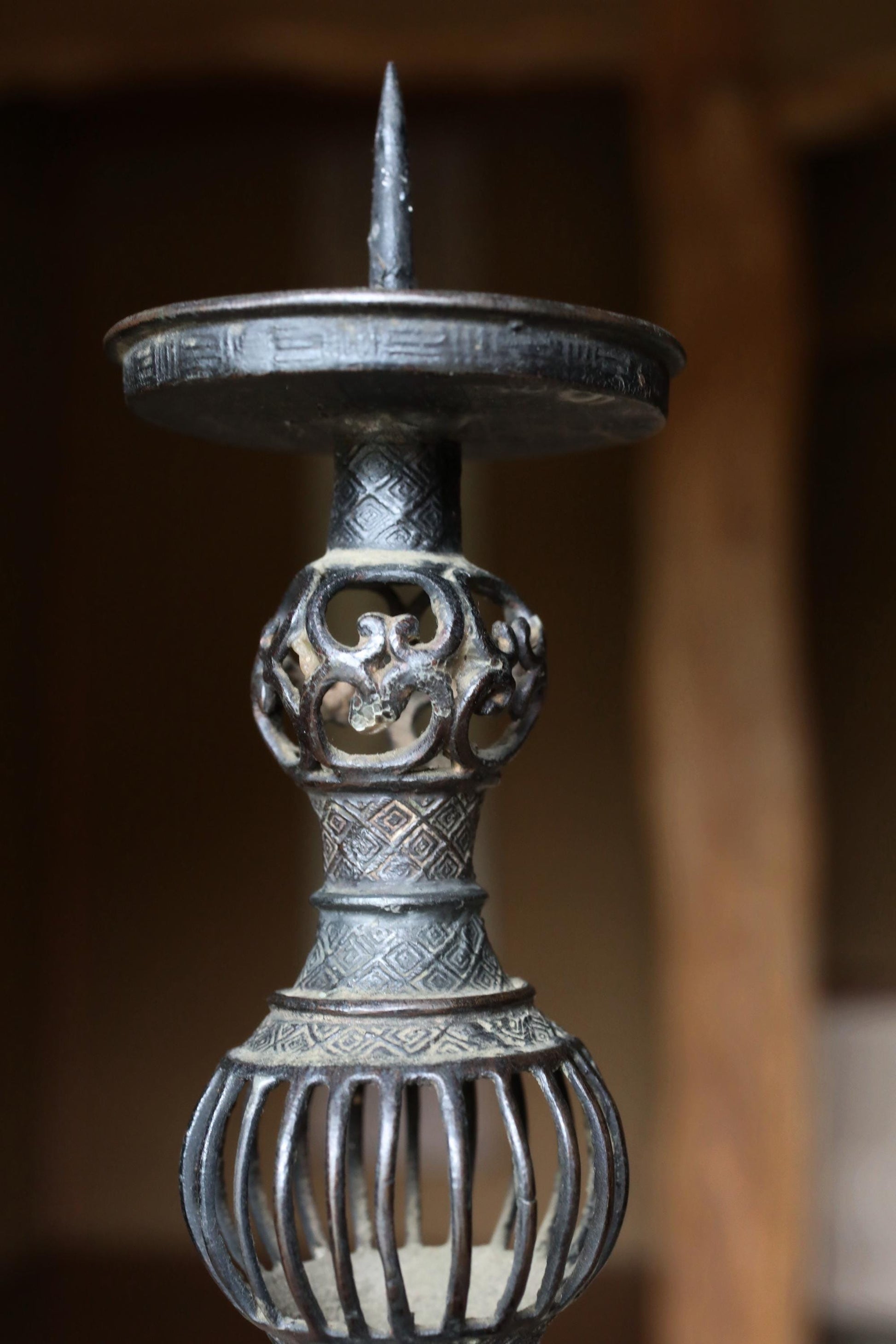 A close-up view of an ornate, metal candlestick with intricate designs and a pointed top.
