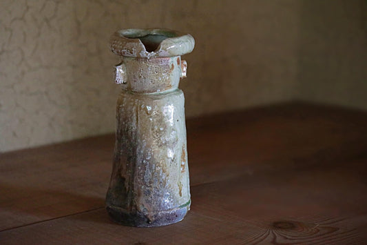 An old, weathered ceramic vase with a distinctive shape sits on a wooden surface.