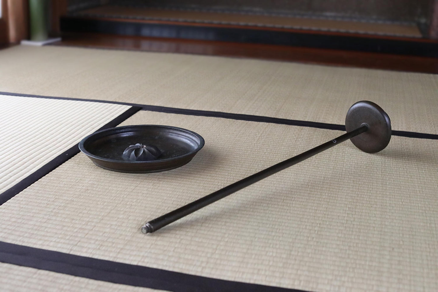 a black metal object, possibly a tool or utensil, lying on a beige mat or rug.