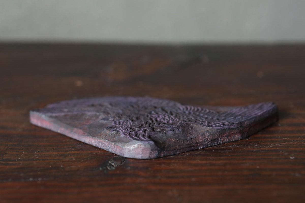 A close-up image of a dark purple, textured object, possibly a piece of wood or a stone, resting on a wooden surface.