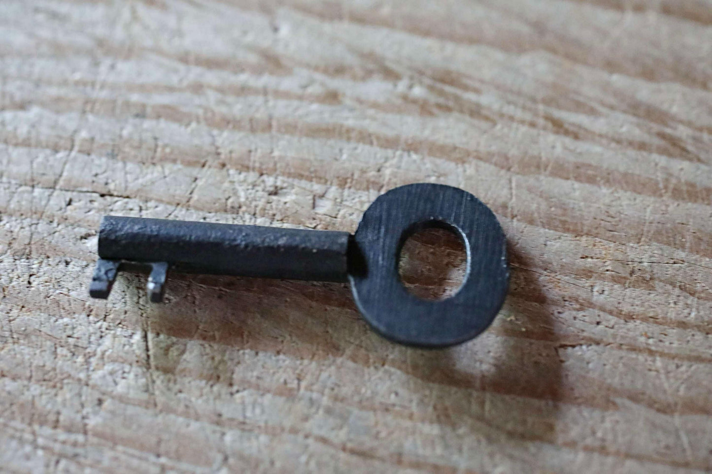 A black metal key with a circular hole is lying on a wooden surface.