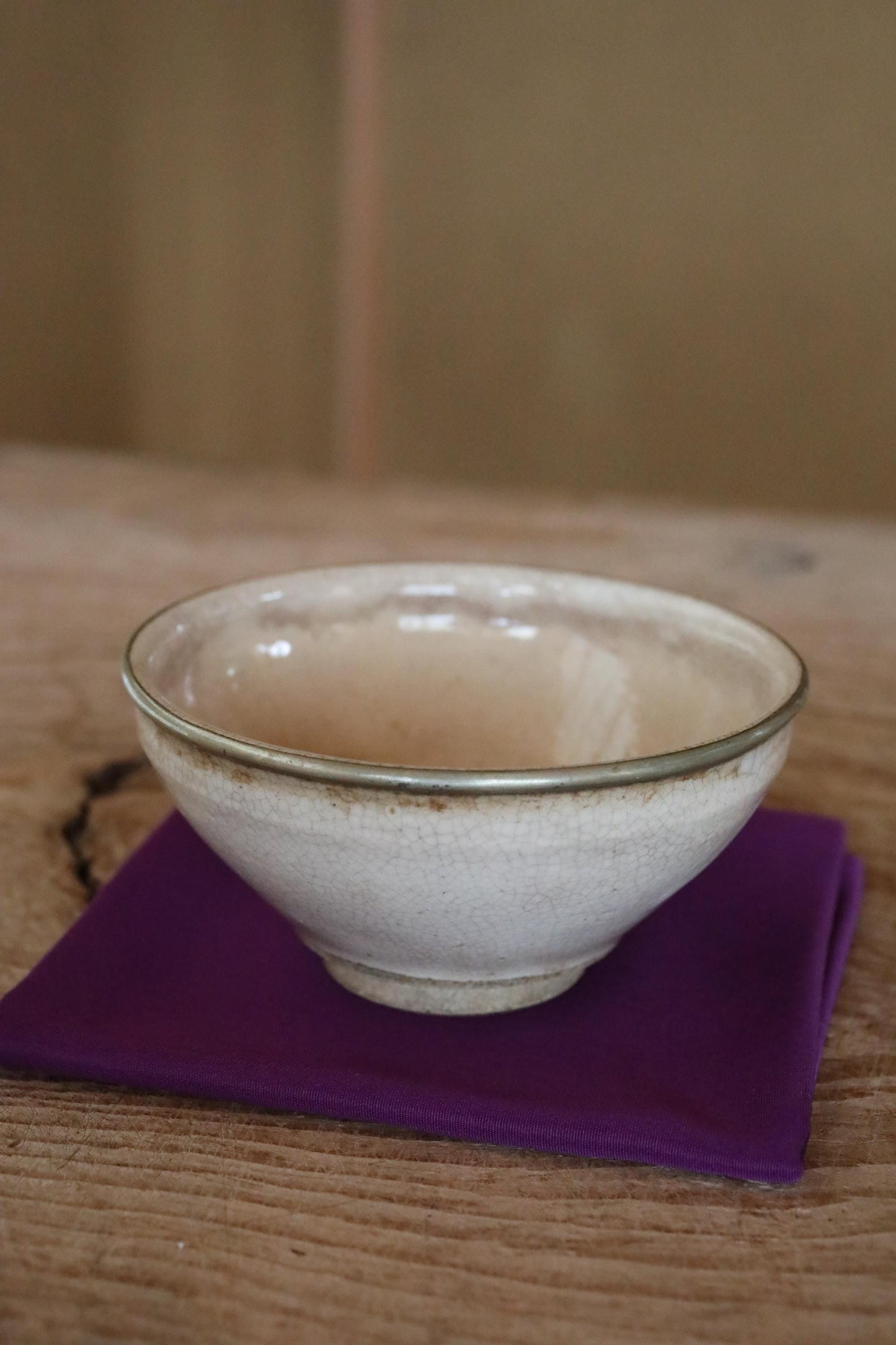 A white ceramic bowl with a textured rim sits on a purple napkin on a wooden table.