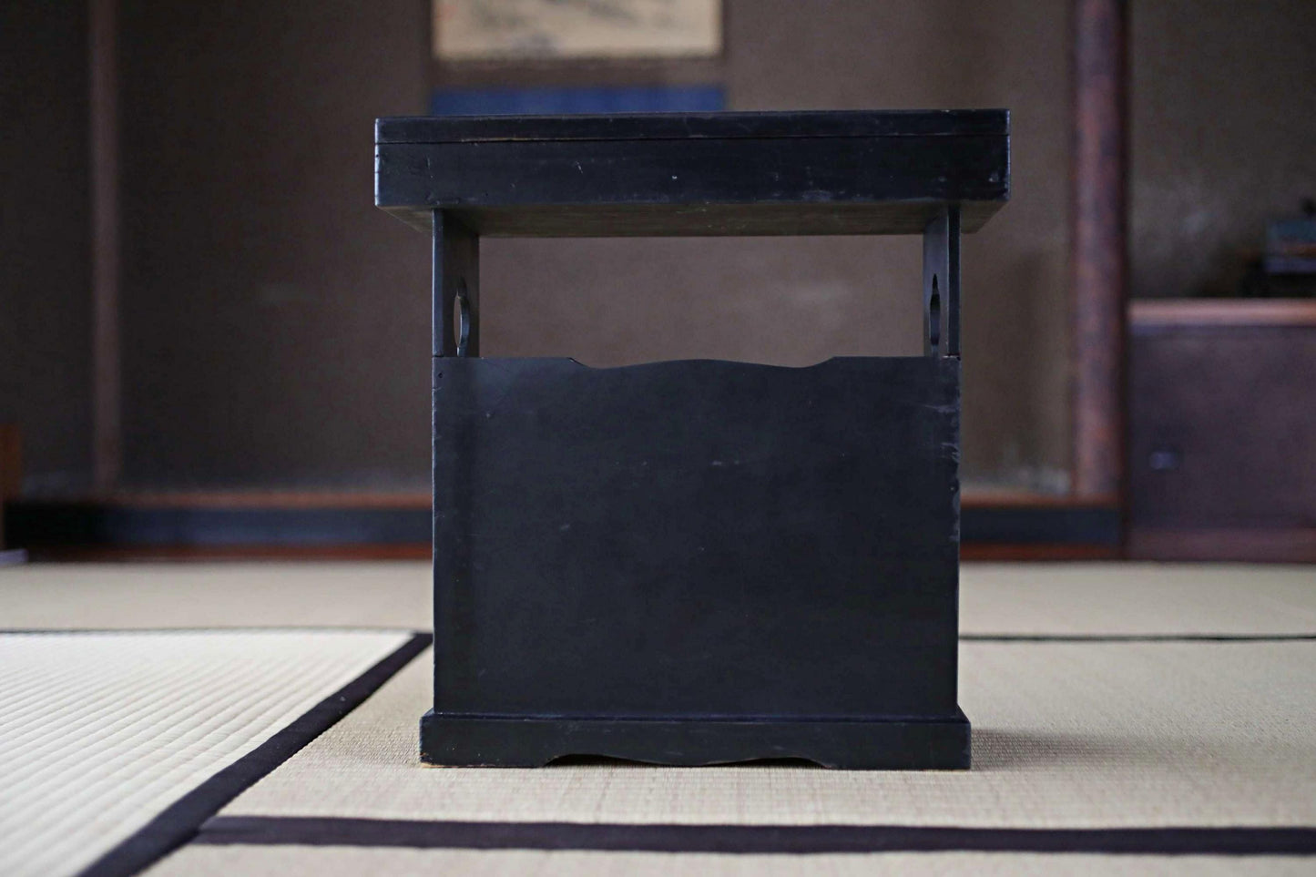 A black wooden table with a shelf on top, placed on a tatami mat.