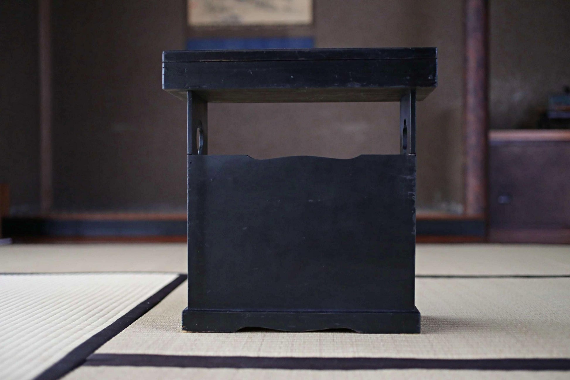 A black wooden table with a shelf on top, placed on a tatami mat.