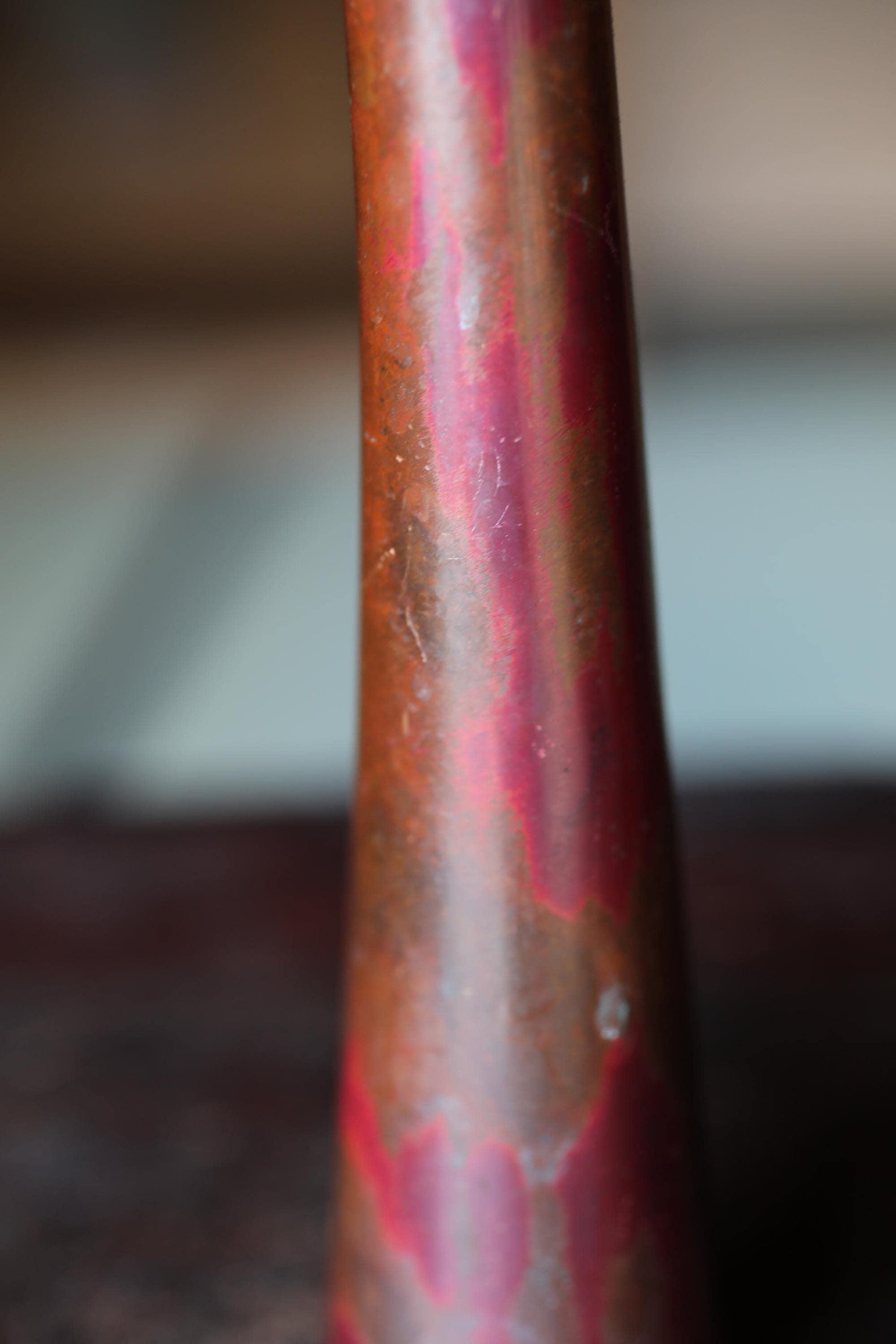 A close-up image of a reddish-brown metal object, possibly a vase or container, with a textured surface.