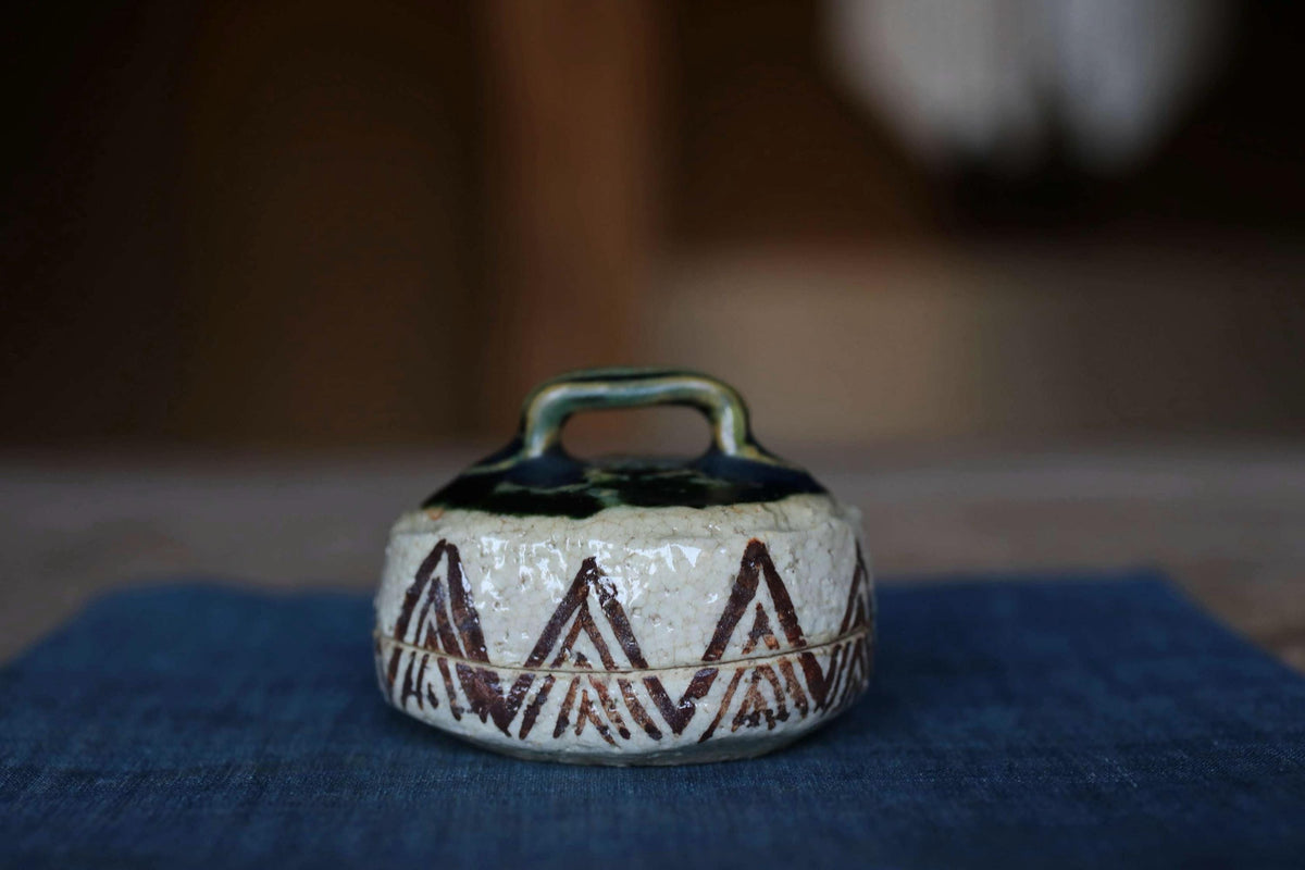 A ceramic container with a handle and a decorative pattern on its surface, placed on a blue cloth.