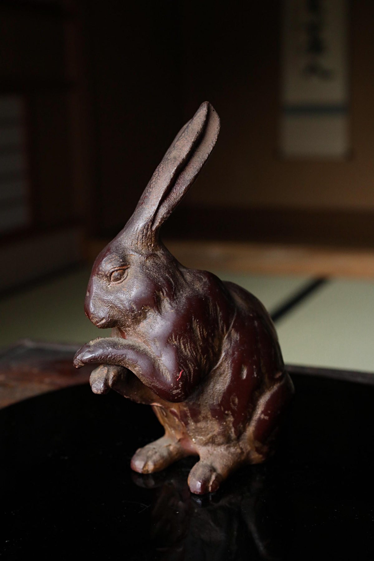 A dark brown, weathered metal rabbit figurine is sitting on a black surface.