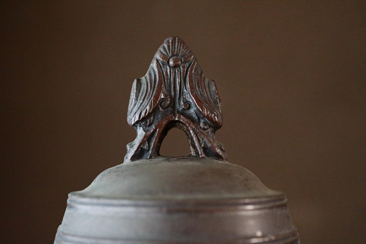 A close-up view of a decorative metal object, possibly a bell or a piece of pottery, with a detailed design on its top.