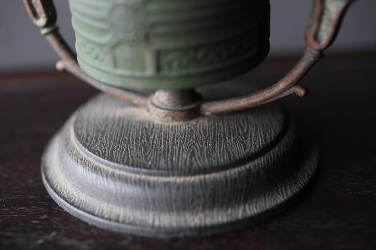 A close-up view of a metal object, possibly a piece of furniture or a decorative item, with a textured surface and a greenish-brown color.
