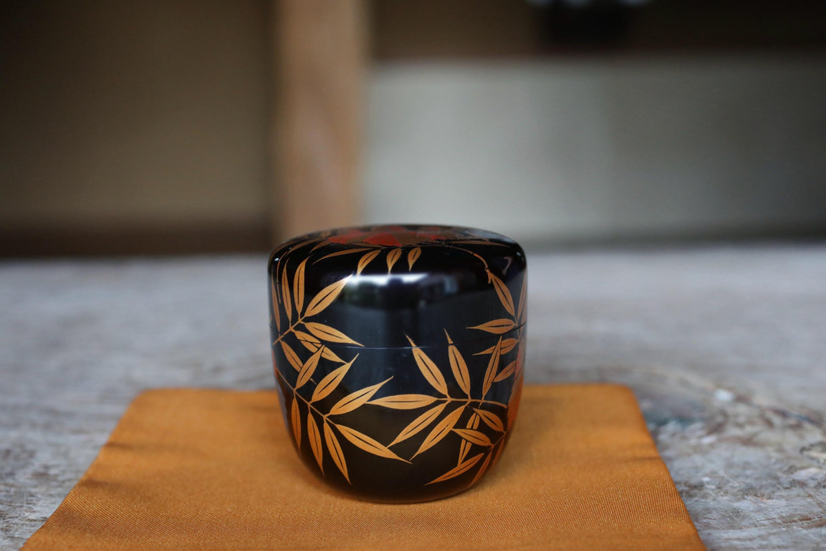 A black ceramic container with a gold leaf design sits on a wooden surface.