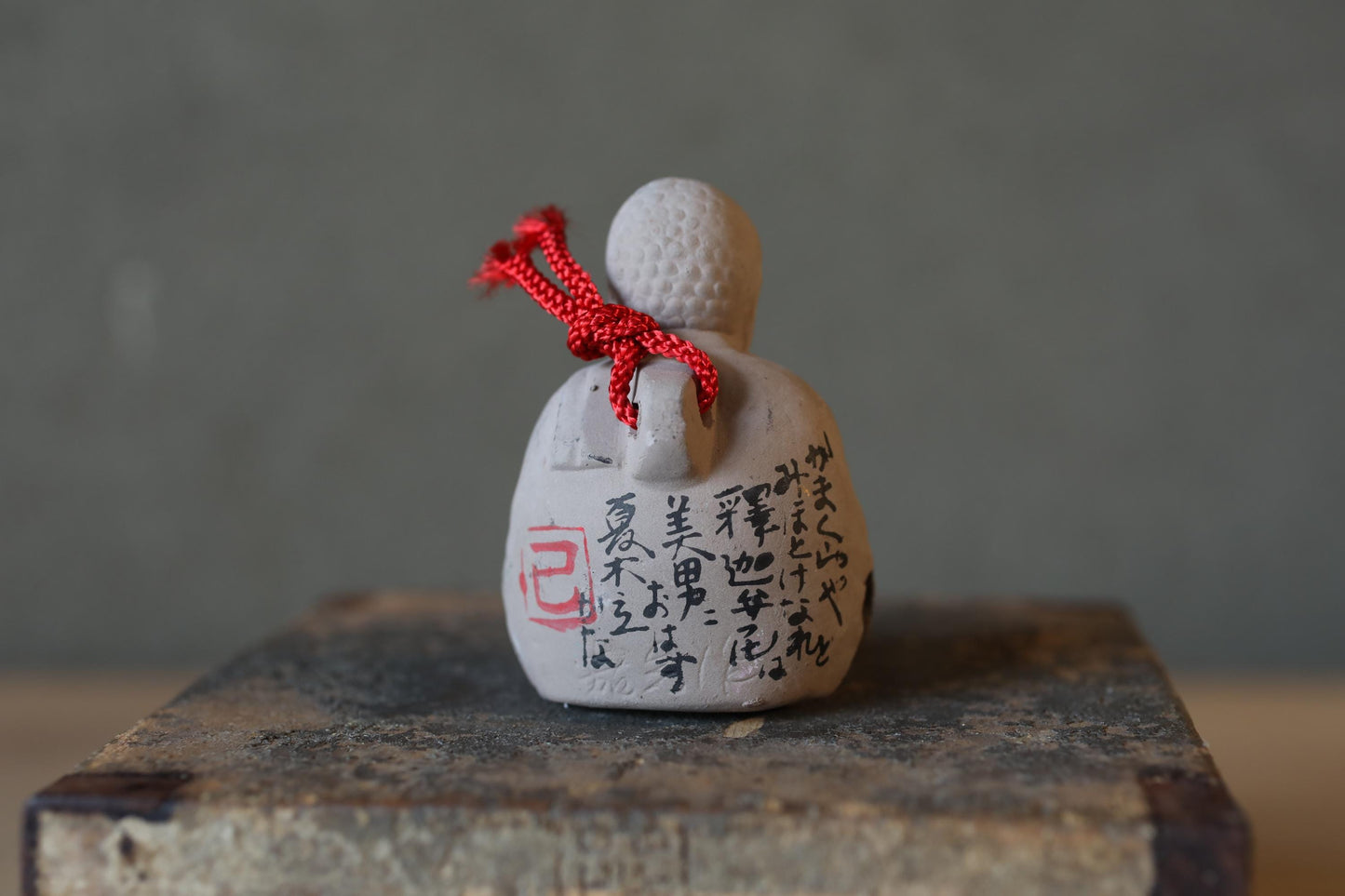 A small ceramic figurine with a red string tied around it, featuring Japanese characters on its surface.