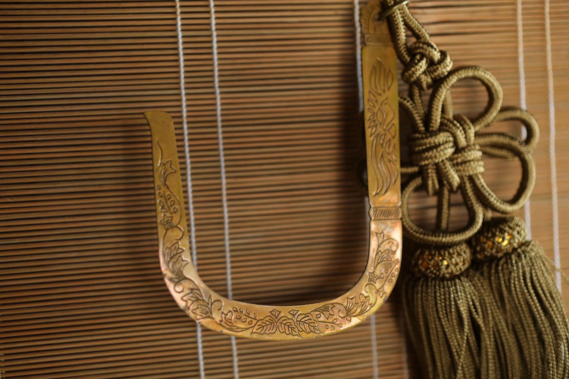 a decorative brass letter 'U' with intricate floral designs, hanging on a wooden blind.