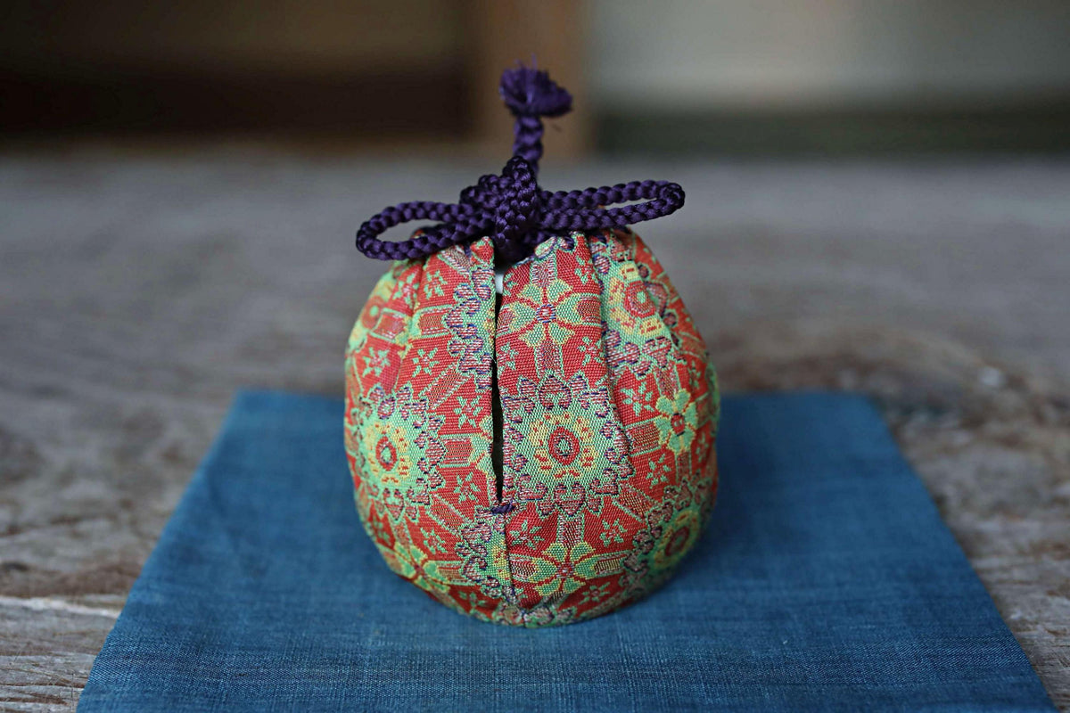 A colorful, patterned ball-shaped object with a purple string tied around it, placed on a blue cloth.