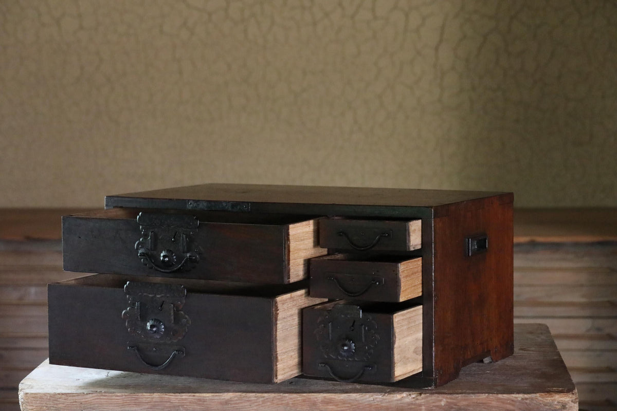 A dark wooden cabinet with six drawers, featuring metal handles and knobs, sits on a wooden surface against a textured wall.