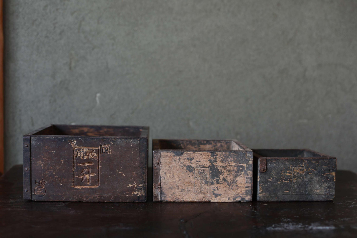 Three old, weathered wooden boxes sit on a dark surface against a gray background.