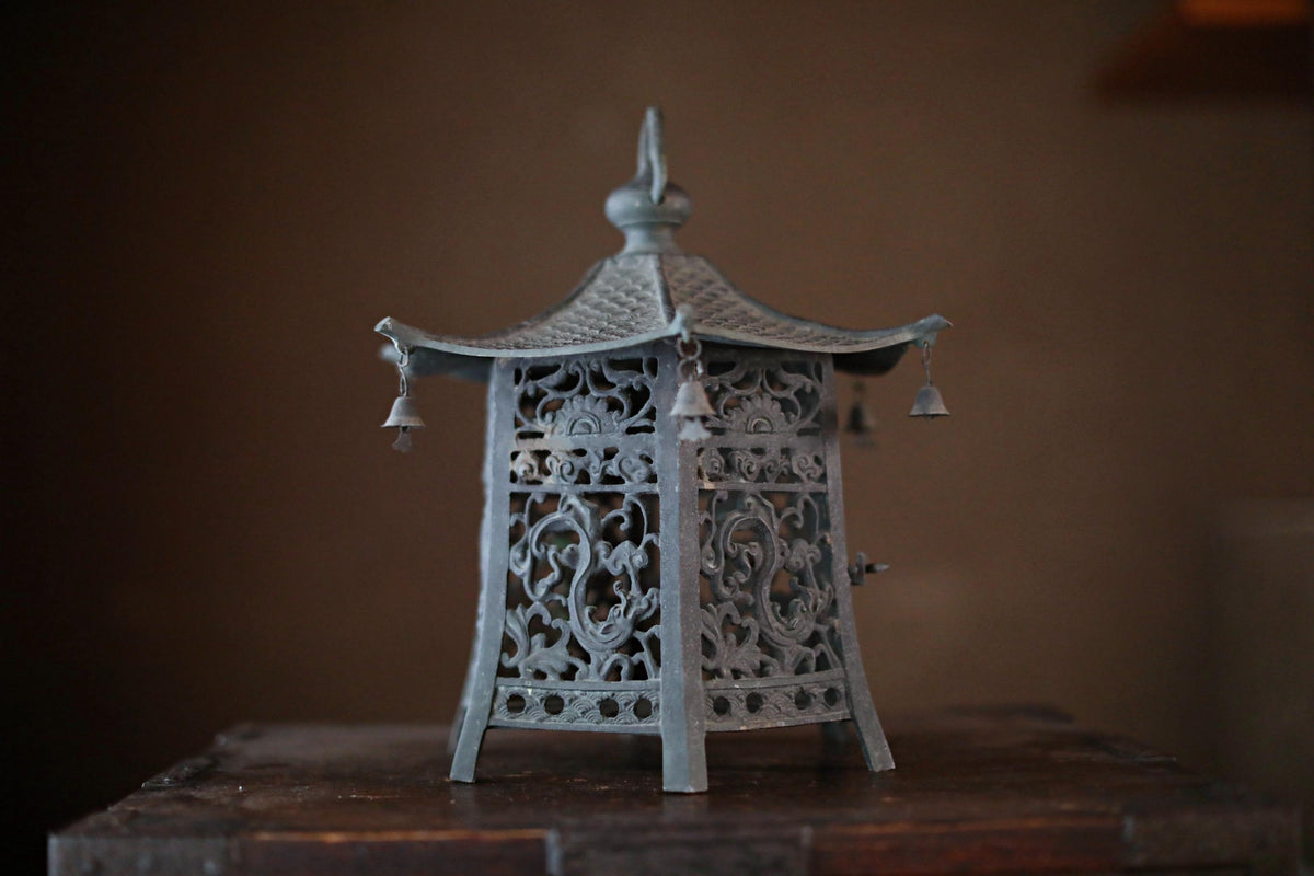 A decorative metal lantern with intricate designs and hanging bells sits on a wooden surface.
